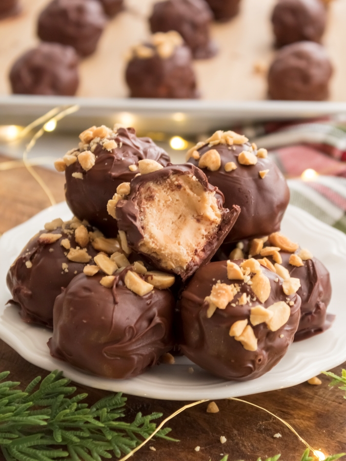 Chocolate Covered Peanut Butter Balls plated with a baking sheet full of more PB Balls in the background