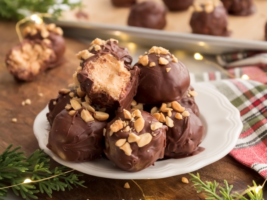 Chocolate Covered Peanut Butter Balls on a plate with a bite taken out of one of the PB balls and a tray of more treats in the background