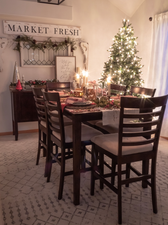 Dining room decorated for Christmas and lit up at night by the glow of a Christmas tree and the candles set on the red and white gingerbread themed tablescape.