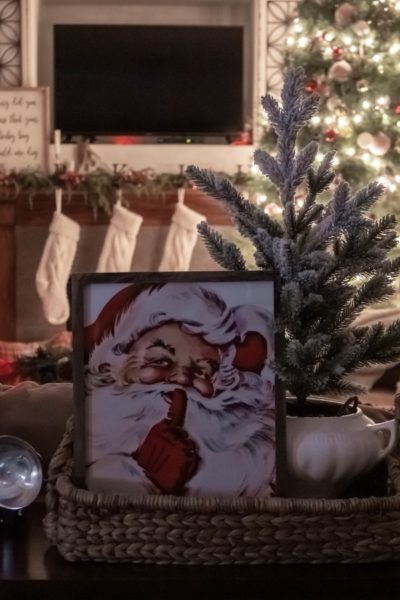 View of Christmas living room at night with a fireplace and tree in the background and a Santa picture and mini tree displayed on a table