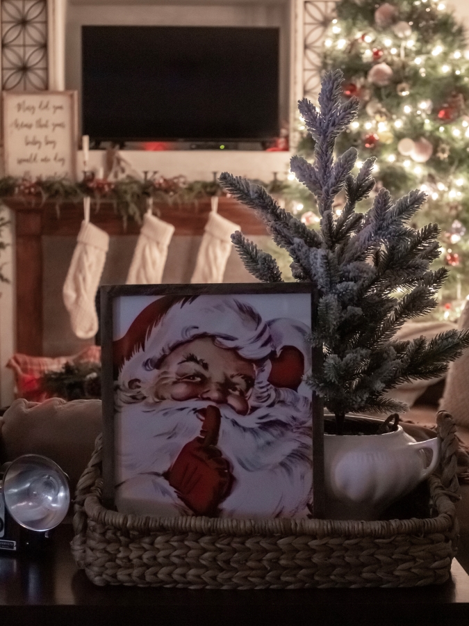 View of Christmas living room at night with a fireplace and tree in the background and a Santa picture and mini tree displayed on a table