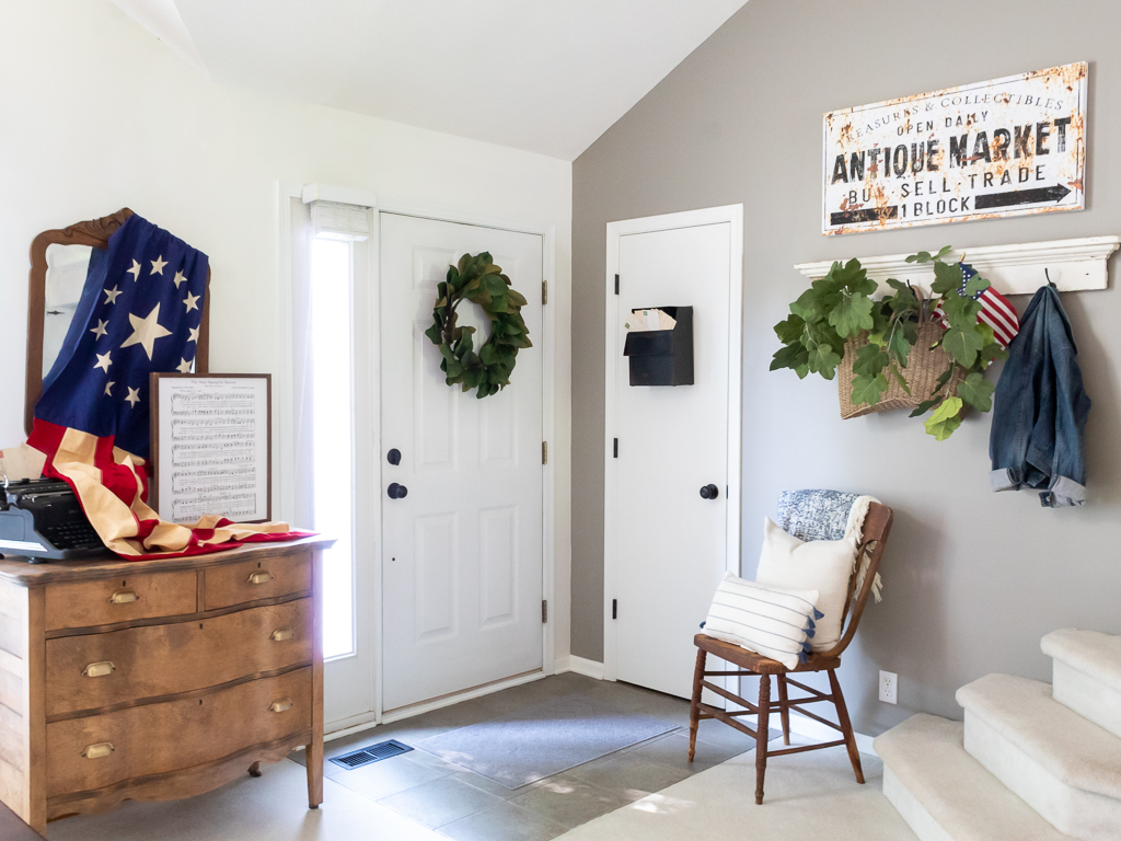 Front entry decorated for summer with patriotic decor and a vintage flag draped over a mirror - Red White And Blue Summer Home Tour - Midwest Life and Style Blog