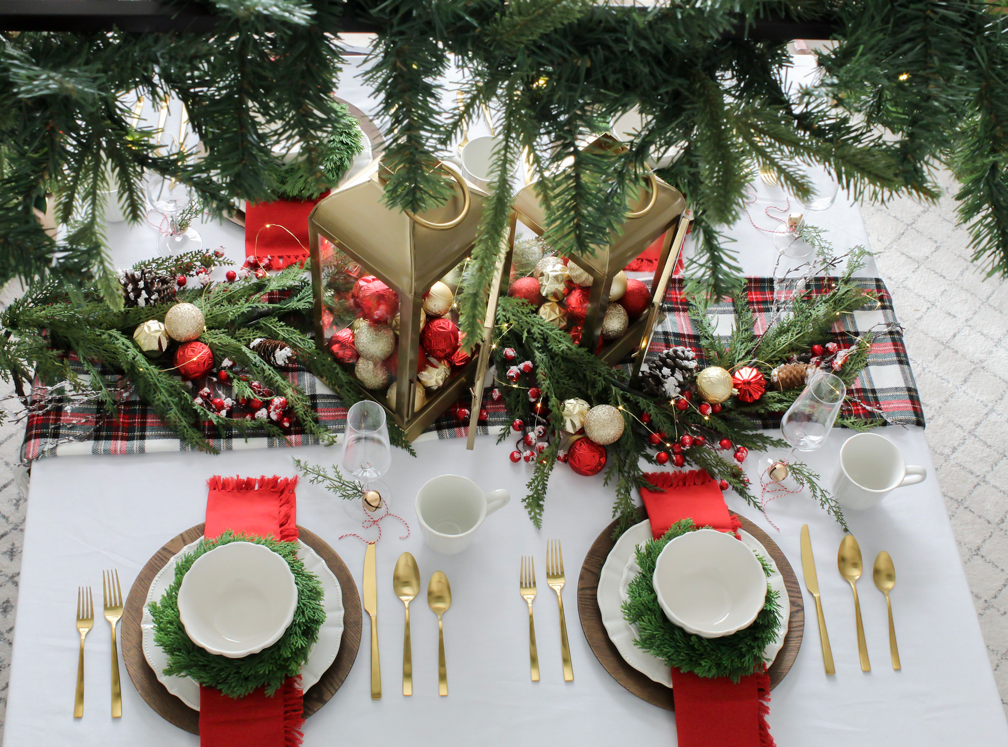 Simple and Festive Christmas Centerpiece Ideas - Overhead View of Gold Lanterns with Red and Gold Christmas Ornaments, Greenery, Plaid Table Runner, and Twinkle Lights