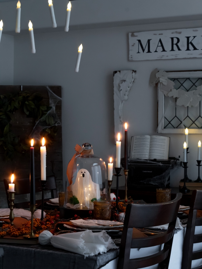 DIY ghost under a cloche lit up, surrounded by candles as part of a rustic, elegant Halloween tablescape