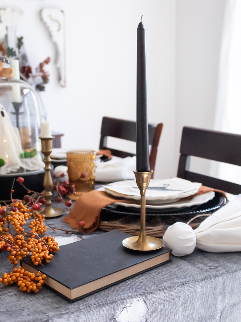 Vintage brass candlestick holders with black cnadles stacked on books on a Halloween table