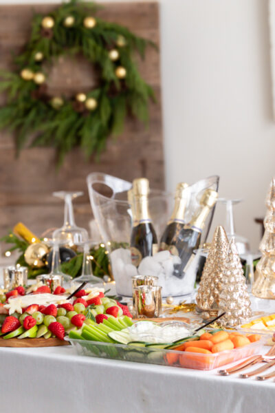 A festive grazing table set up on the dining room table with a charcuterie board, relish tray, and red and green fruit wreath for a New Year's eve party.