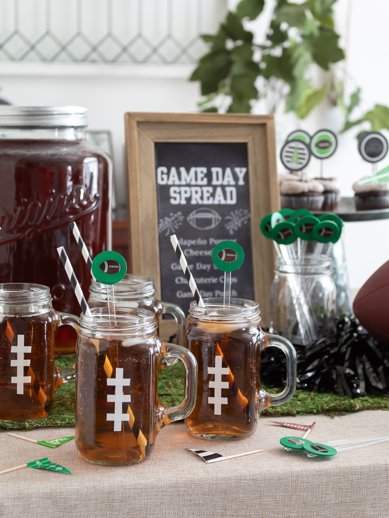 Drink station with mason jar mugs decorated to look like footballs and DIY football drink stir sticks for a Super Bowl party