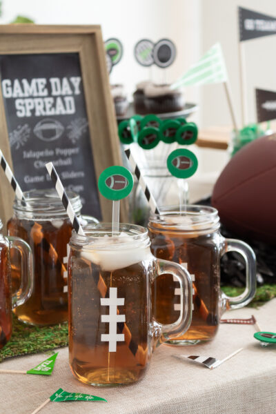 Drink station with mason jar mugs decorated to look like footballs and black and white paper straws with DIY football drink stir sticks for a Super Bowl party