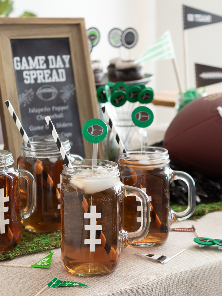 Drink station with mason jar mugs decorated to look like footballs and black and white paper straws with DIY football drink stir sticks for a Super Bowl party