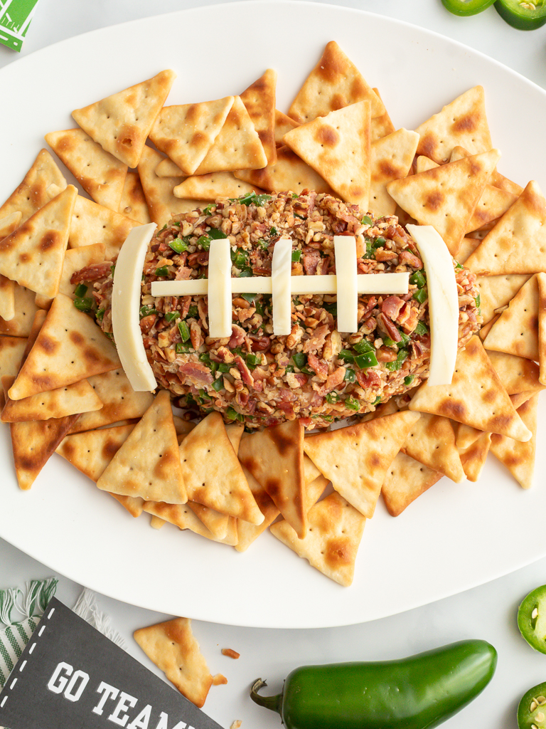 Football shaped jalapeno popper cheeseball with bacon and football laces made of cheese served on a tray with crackers