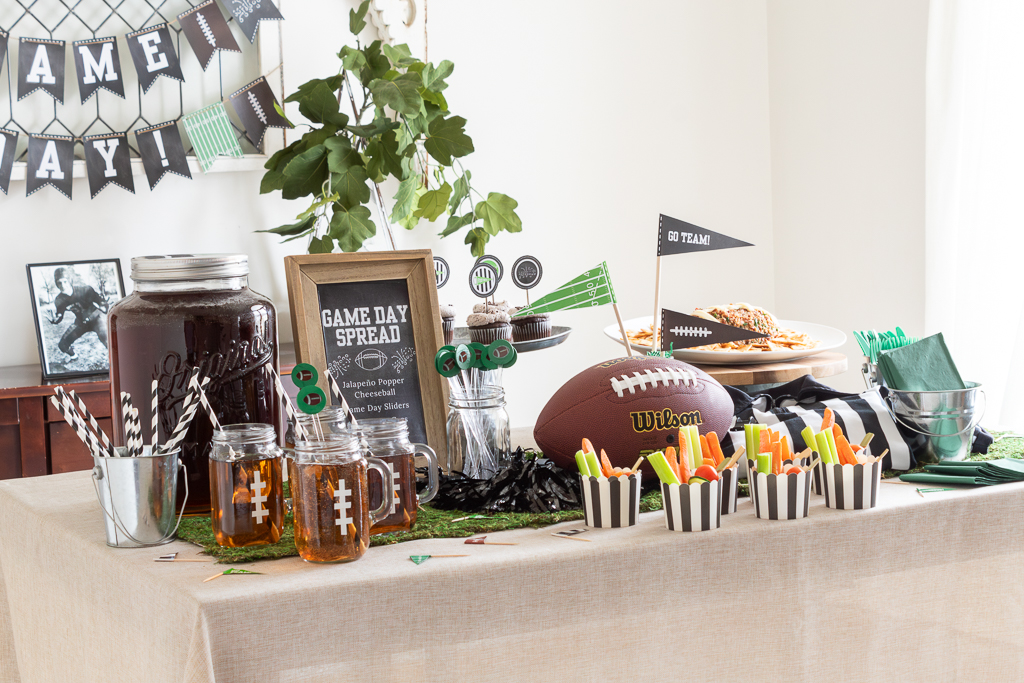 Dining room table decorated with green and black Super Bowl-themed tablescape  with food and drink stations and a football and referee jersey centerpiece and free game day printables for a Big Game party