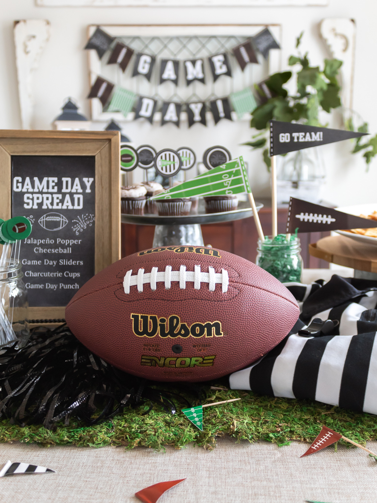 Centerpiece for a Super Bowl party tablescape with a football, chalkboard menu, pompoms, referee jersey, and free printable game day party pennants. 