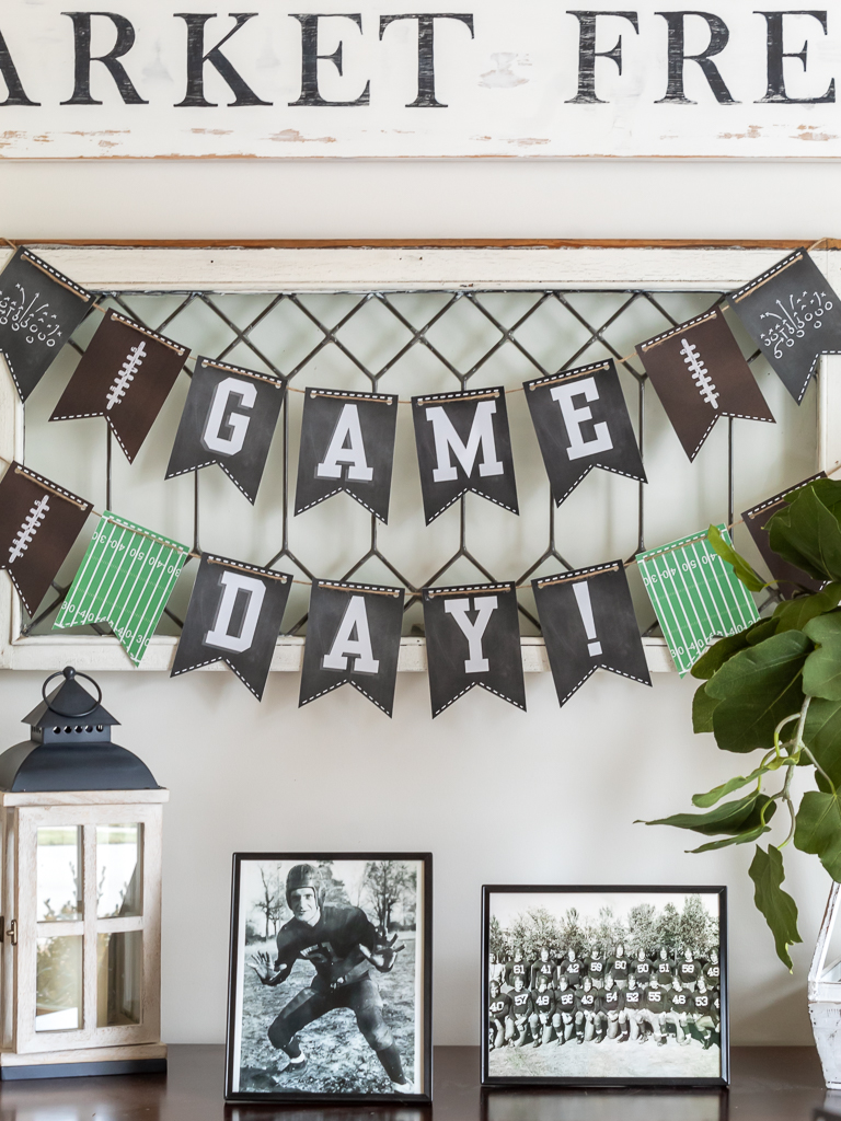 Free game day printable party banner dislayed on a vintage window for a football tailgate or watch party for the Super Bowl with a console table with old black and white photos of football players