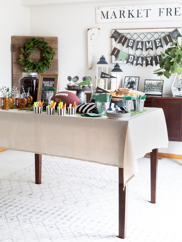 Dining room table decorated with green and black Super Bowl-themed tablescape with a footbal and referee jersey centerpiece for a Big Game party