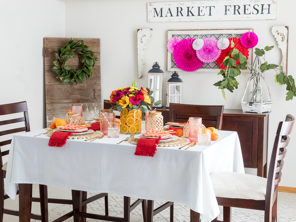 Dining Room Styled for a Chinese New Year Dinner Party with Bambo Lanterns, Woven Placemat with Red and Coral Linens and Brightly Colored Flowers with Sliced Oranges