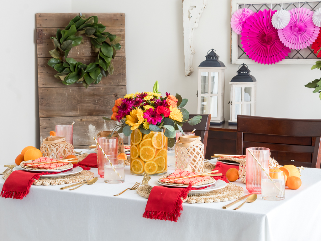 Dining Room Styled for a Chinese New Year Dinner Party with Bambo Lanterns, Woven Placemat with Red and Coral Linens and Brightly Colored Flowers with Sliced Oranges