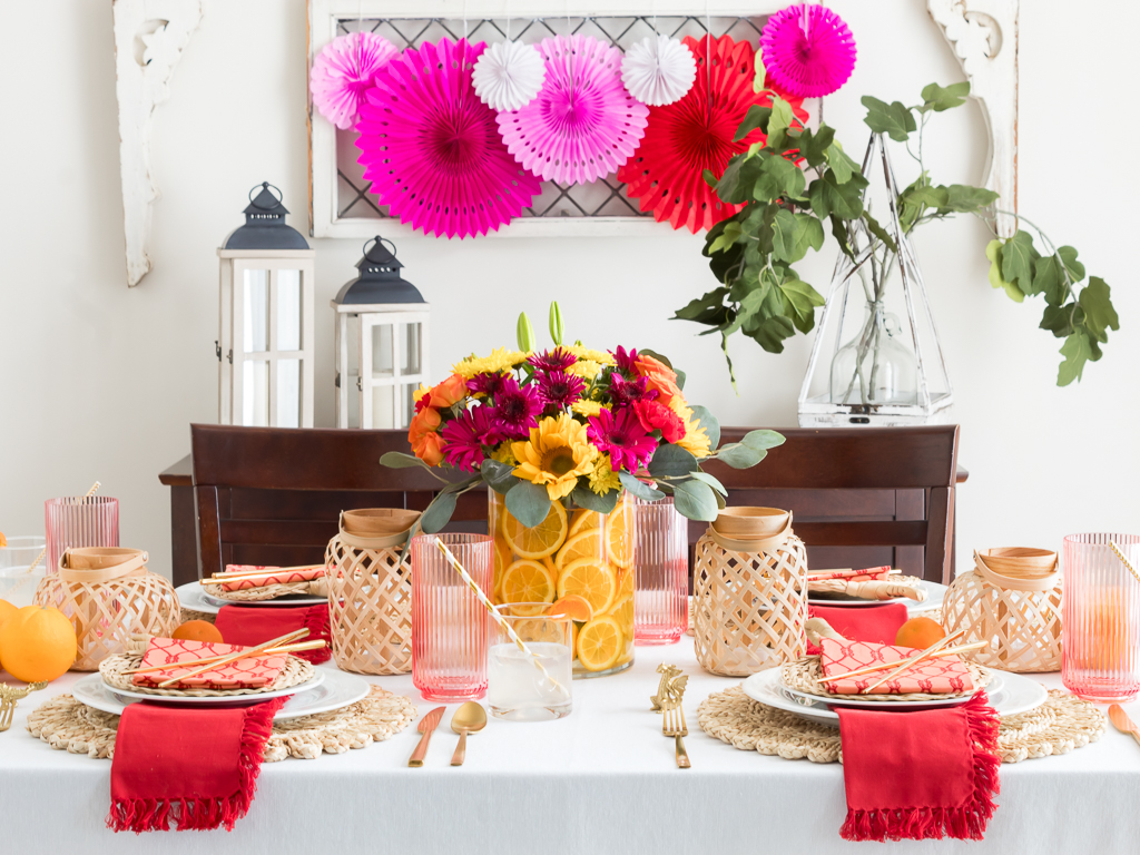 Dining Room Styled for a Chinese New Year Dinner Party with Bambo Lanterns, Woven Placemat with Red and Coral Linens and Brightly Colored Flowers with Sliced Oranges