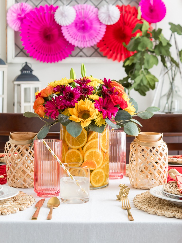 Dining Room Styled for a Chinese New Year Dinner Party with Bambo Lanterns, Woven Placemat with Red and Coral Linens and Brightly Colored Flowers with Sliced Oranges