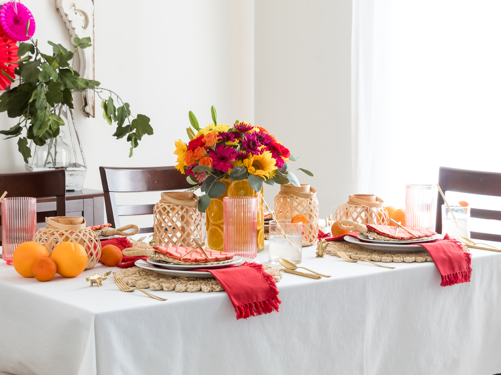 Dining Room Styled for a Chinese New Year Dinner Party with Bambo Lanterns, Woven Placemat with Red and Coral Linens and Brightly Colored Flowers with Sliced Oranges