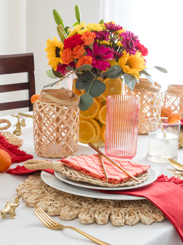 Bright and colorful spring tablescape for a Chinese dinner party with pink, red, gold, and a centerpiece with spring flowers and sliced mandarin oranges