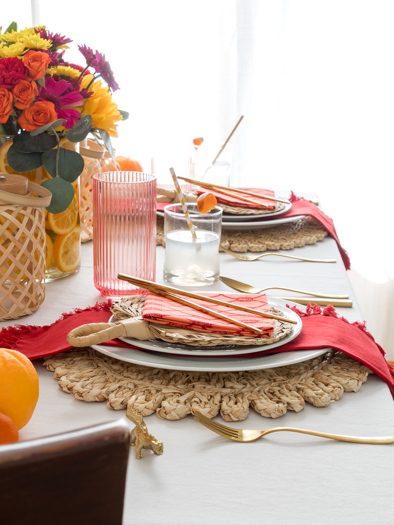 Dining Room Styled for a Chinese New Year Dinner Party with Bambo Lanterns, Woven Placemat with Red and Coral Linens and Brightly Colored Flowers with Sliced Oranges