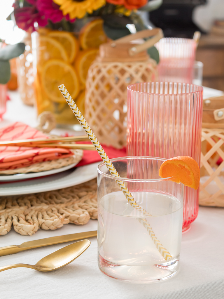 Dining Room Styled for a Chinese Mandarin Mule Styled on a New Year Dinner Party with Bambo Lanterns, Woven Placemat with Red and Coral Linens and Brightly Colored Flowers with Sliced Oranges