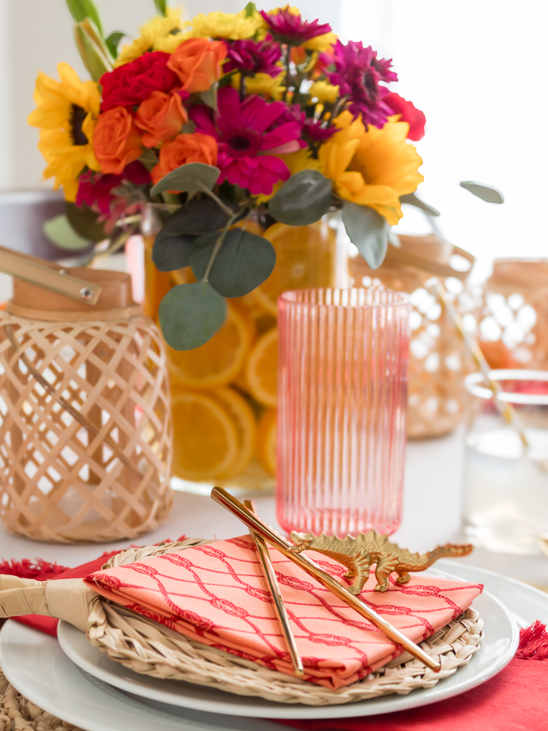 Dining Room Styled for a Chinese New Year Dinner Party with Bambo Lanterns, Woven Placemat with Red and Coral Linens and Brightly Colored Flowers with Sliced Oranges