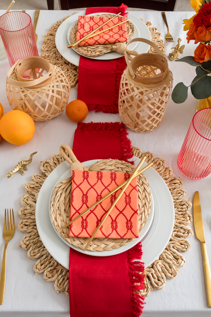 Dining Room Styled for a Chinese New Year Dinner Party with Bambo Lanterns, Woven Placemat with Red and Coral Linens and Brightly Colored Flowers with Sliced Oranges