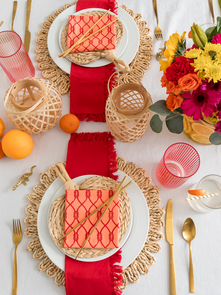 Dining Room Styled for a Chinese New Year Dinner Party with Bambo Lanterns, Woven Placemat with Red and Coral Linens and Brightly Colored Flowers with Sliced Oranges