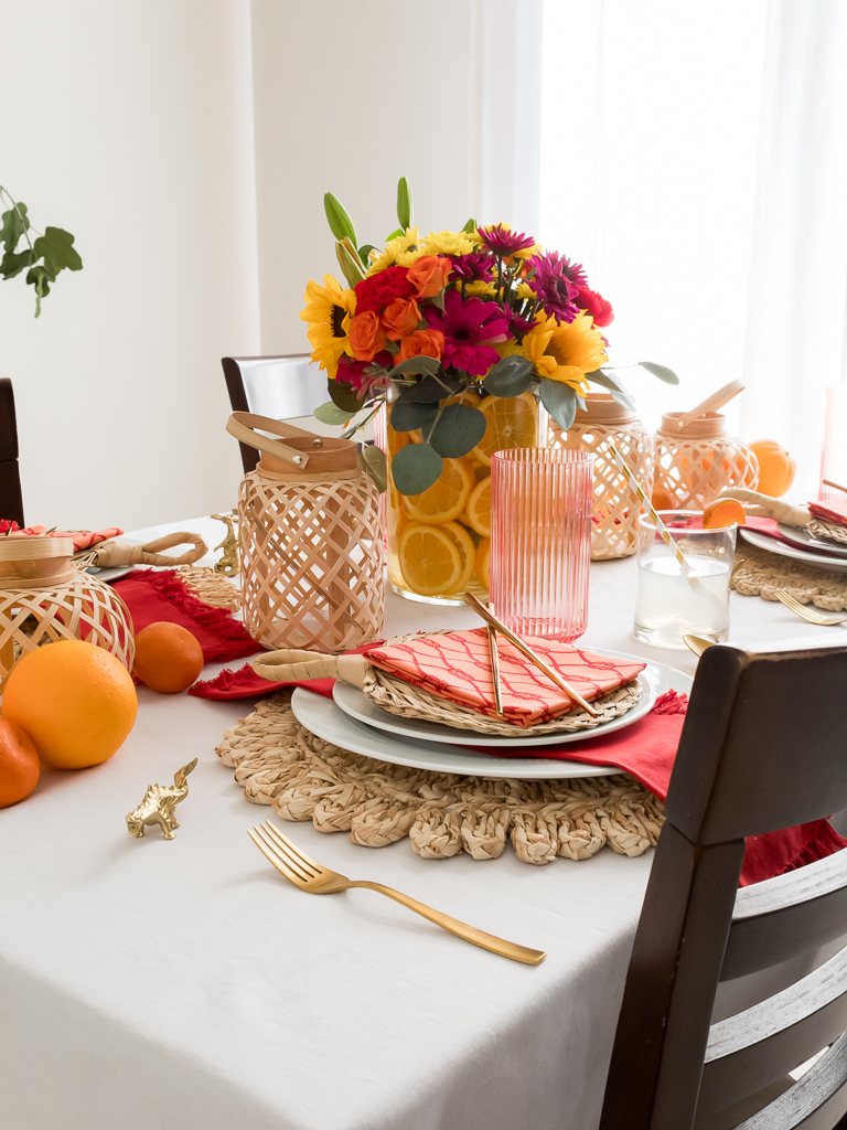 Dining Room Styled for a Chinese New Year Dinner Party with Bambo Lanterns, Woven Placemat with Red and Coral Linens and Brightly Colored Flowers with Sliced Oranges