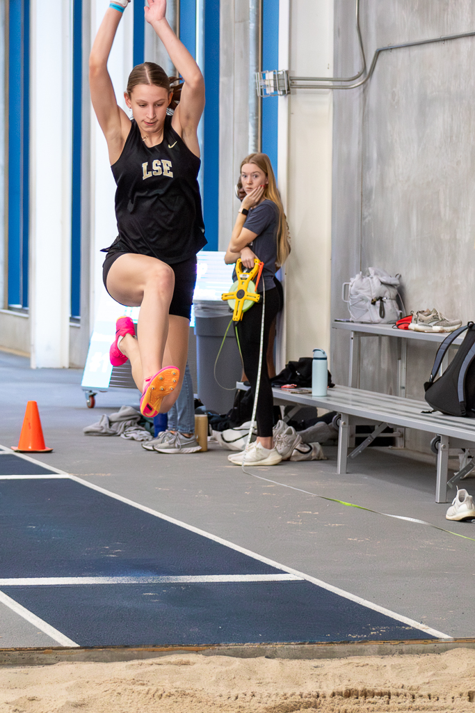 Young female athlete doing triple jump and juping into the sand pit