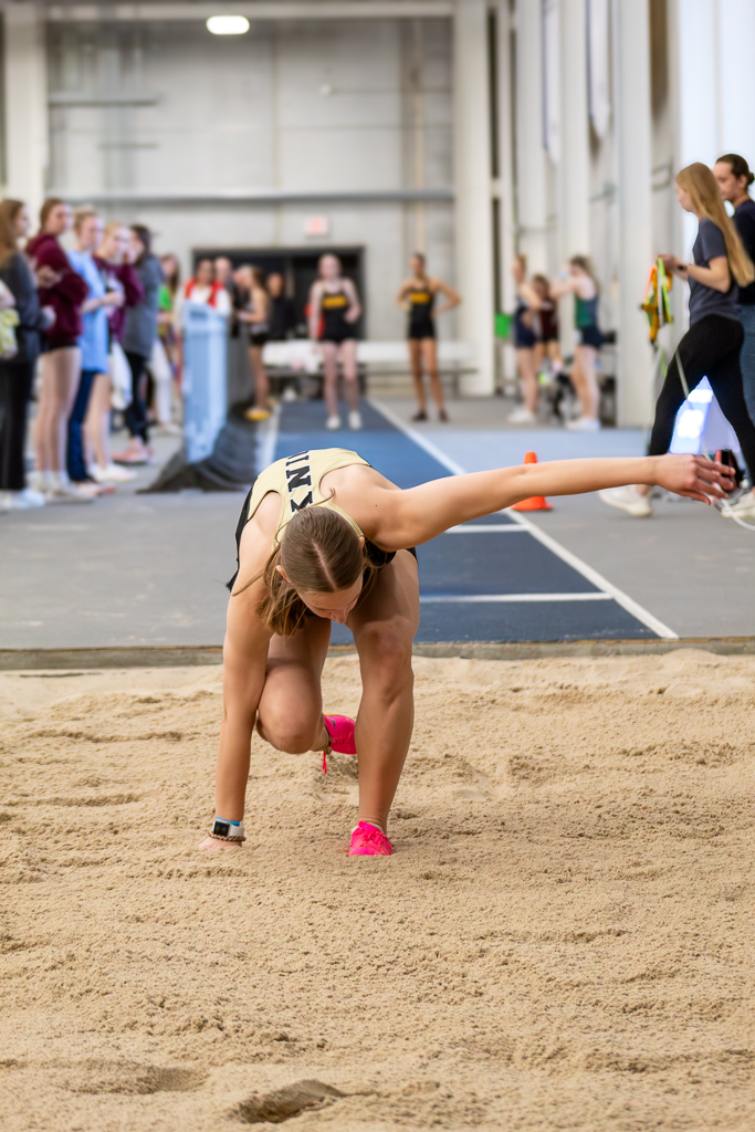 Young female athlete doing triple jump and juping into the sand pit