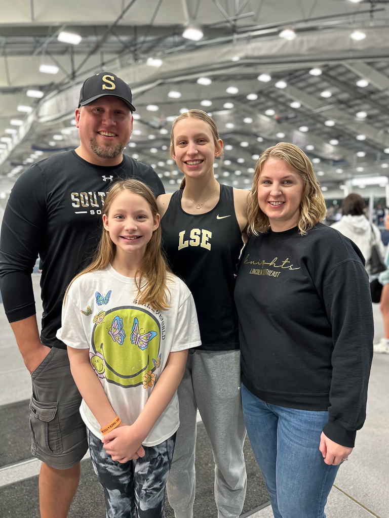 Family of four including mom, dad and two daughters smiling and posing at a track meet