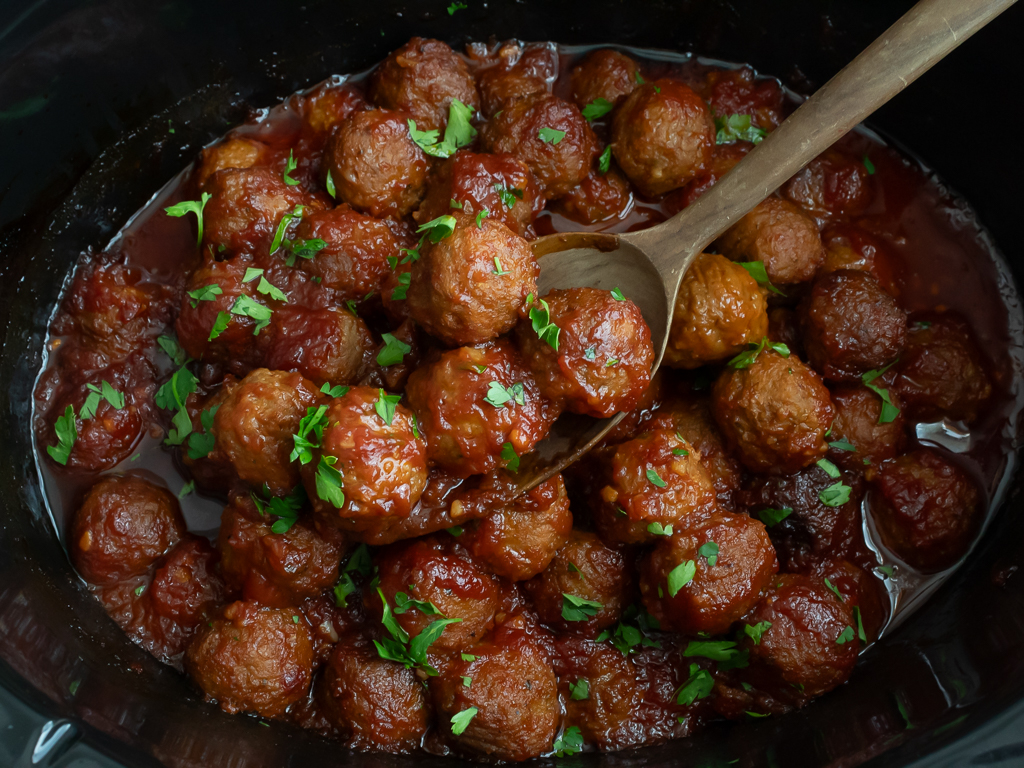 Crockpot Bourbon BBQ Meatballs in the slow cooker displayed on a wooden spoon