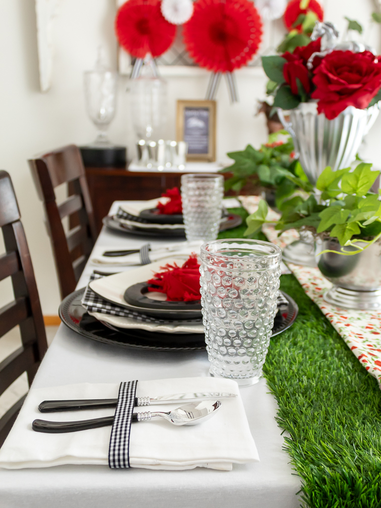 Close up view of black handled silverware, black and white dishes, red rose fold napkins, and hobnail drinking glasses on a tablescape styled for a Kentucky Derby party