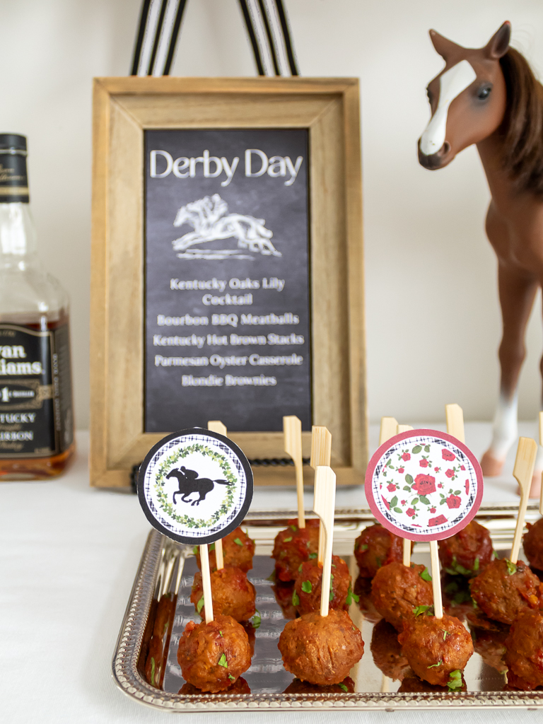 Close up view of crockpot bourbon meatballs dispalyed on a siler tray for a Kentucky Derby party with free printable toothpick party toppers