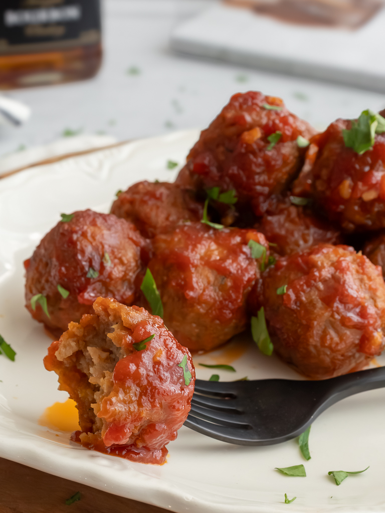 Crockpot Bourbon Meatballs plated on display with one on a fork and a bit taken out of it