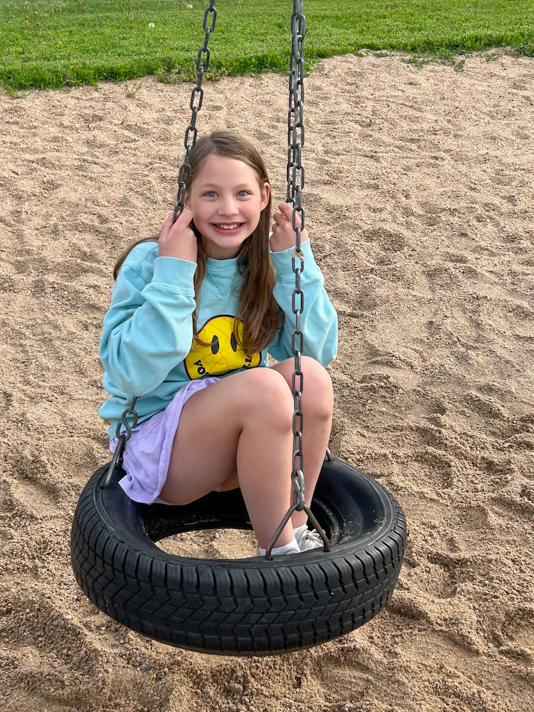 girl in a tire swing at the park smiling