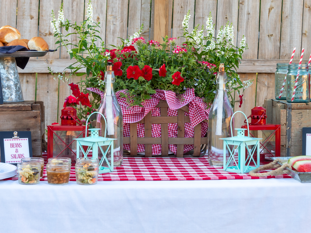 picnic basket filled with flowers and paried with lanterns and diy tiki torches on a cookout table in the backyard