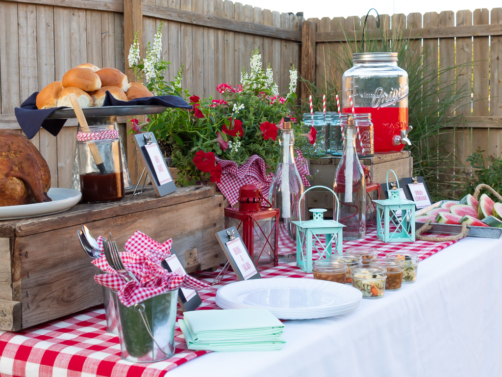 Side view of a cookout buffet table set up in the backyard for summer with smoked chicken, side salads, watermelon and a drink station