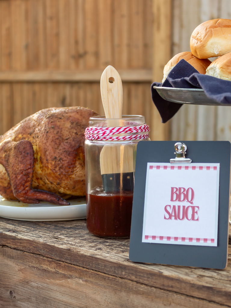 BBQ sauce in a glass jar with a basting brush and smoked beer can chciken on a picnic buffet table 