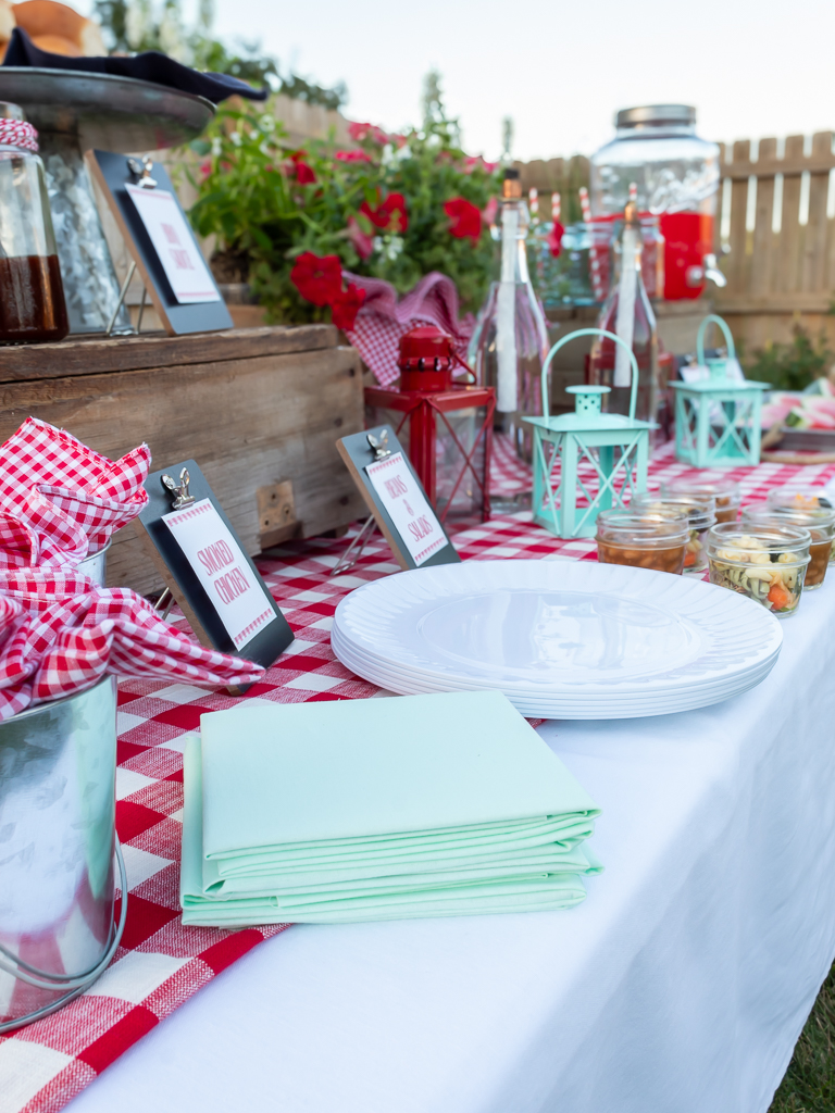 Plastic plates and napkins set up on a food station for a a backyard cookout