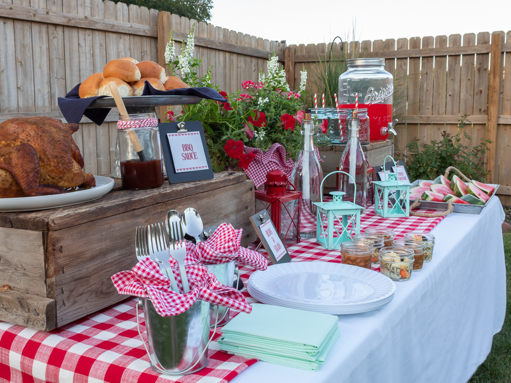 Food on a table for a summer BBQ including smoked beer can chicken, rolls, baked beans, pasta salad, sliced watermelon, and drinks