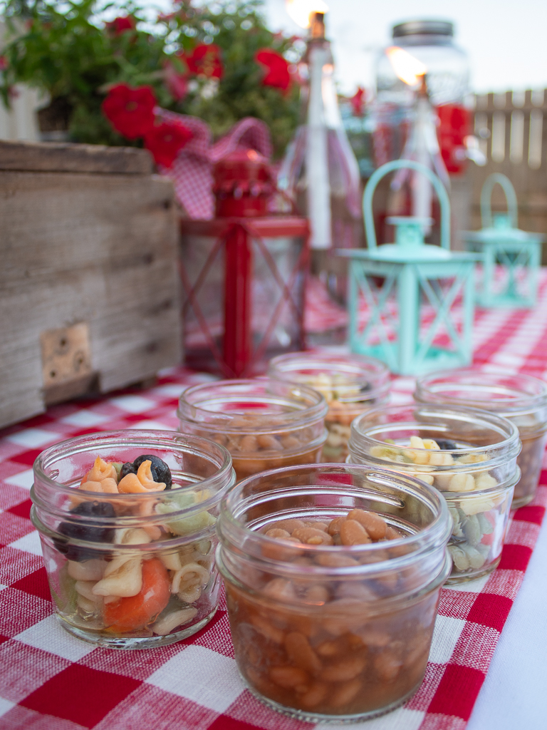 Side salads and baked beans served in mini mason jars for a picnic or a backyard cookout