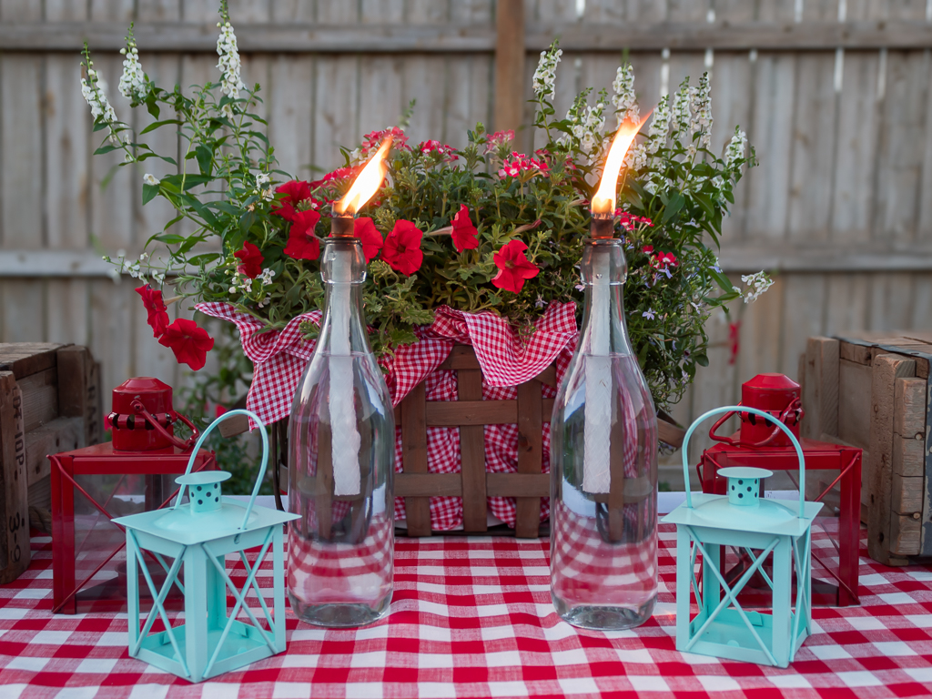 DIY tabletop wine bottle citronella torches lit up on a backyard cookout buffet table