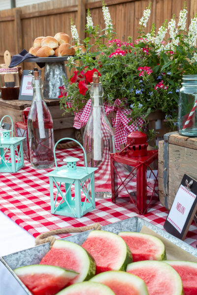 Food buffet set up for a red and white-themed backyard cookout with watermelon, smoked chicken and sides