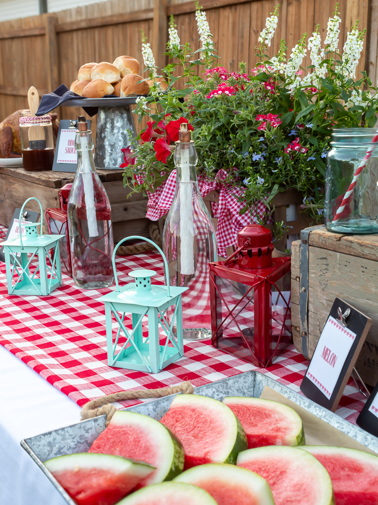 Food buffet set up for a red and white-themed backyard cookout with watermelon, smoked chicken and sides