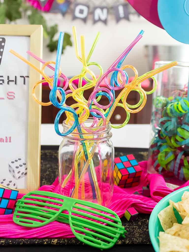 Neon colored crazy straws on a food buffet for an 80s game night party