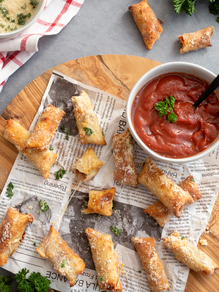 Pizza Rolls made  in the Air Fryer displayed on a wood cutting board with a bowl of pizza sauce for dipping