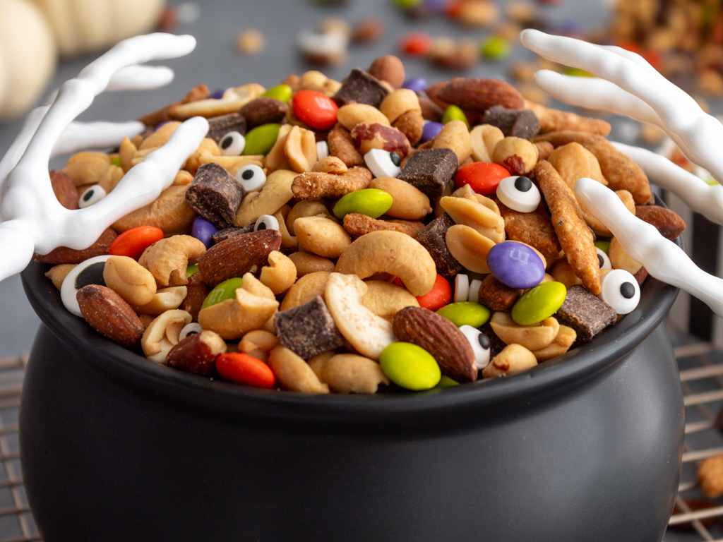 Close up of Halloween Monster Munch Trail Mix with candy eye sprinkles and skeleton hand serving utensils in a caldron bowl